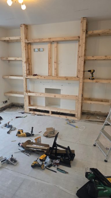 Wooden shelving unit under construction in a messy room with tools scattered around.
