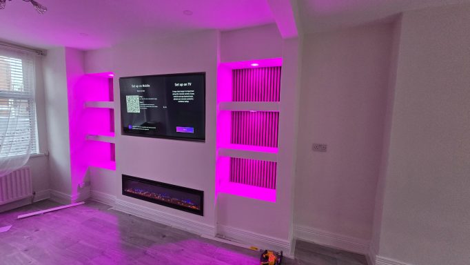 Modern living room with purple LED lighting, wall-mounted TV, and built-in shelves.