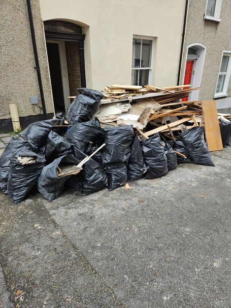 A large pile of black garbage bags and wooden debris on a street.